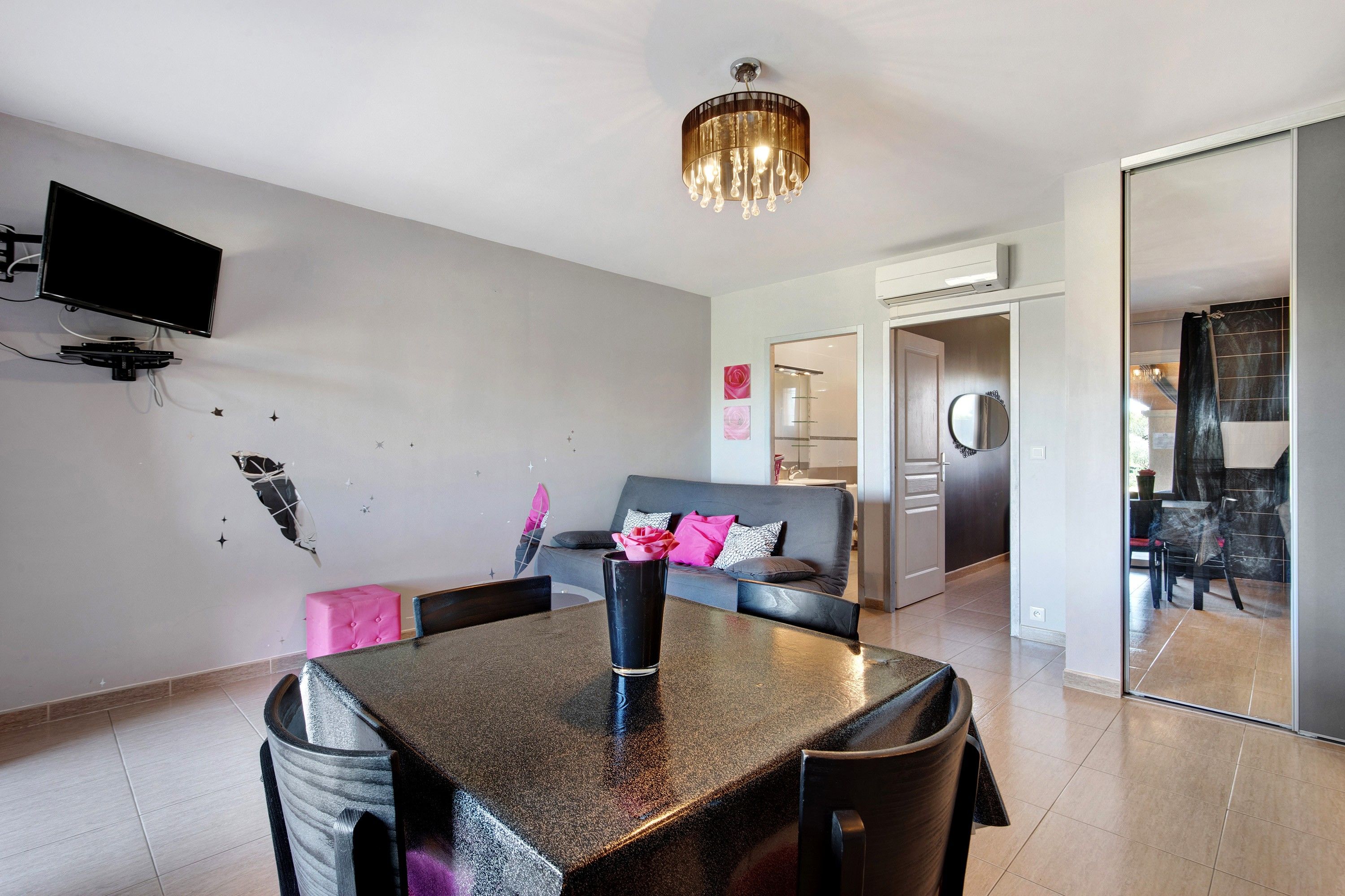 Een moderne woonkamer met een eettafel, bank en een aan de muur bevestigde televisie.