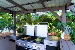 Ein Grill mit mehreren Kochflächen, einem Getränkehalter und einem Drink sowie einer Ananas.