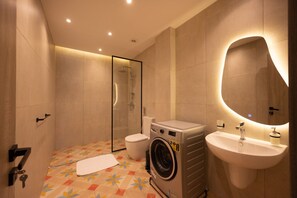 A modern bathroom with a glass-enclosed shower, a washing machine, and a sink with a mirror. - Luxury stay at Degla by Spacey #68 (Cairo)