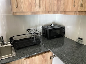 A kitchen with a microwave, a black dish rack, and wooden cabinets.