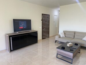 A modern living room with a flat-screen TV on a wooden stand, a beige sofa, and a coffee table with a remote and a box.