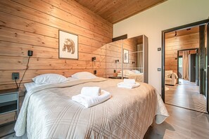 A bedroom with a large bed, wooden walls, a mirror, and a door leading to another room. - Tieva Chalets Levi by Aavalevi (Levi)