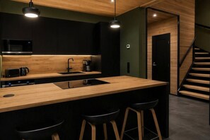 A modern kitchen with a wooden countertop, black bar stools, and a staircase leading to another level. - Tieva Chalets Levi by Aavalevi (Levi)