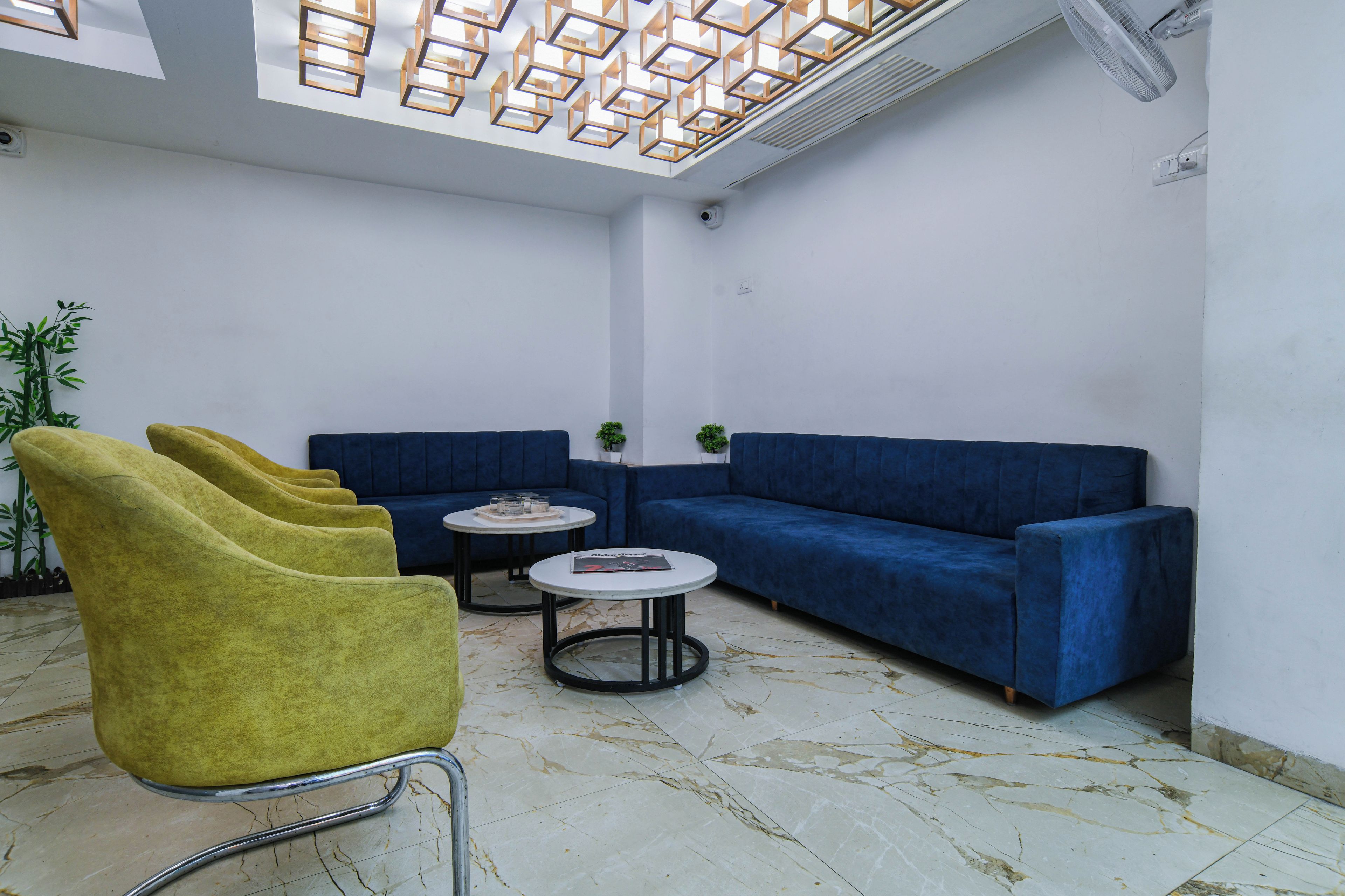 Un'area lounge moderna con un divano blu, poltrone gialle e due tavolini.