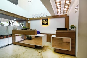 A hotel reception area with a reception desk, a wall clock, and a sign indicating the hotel name. - Hotel The Grand (Indore)