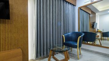 Habitación de hotel con pared de paneles de madera, un sillón azul, una mesita de vidrio y un espejo que refleja la habitación.
