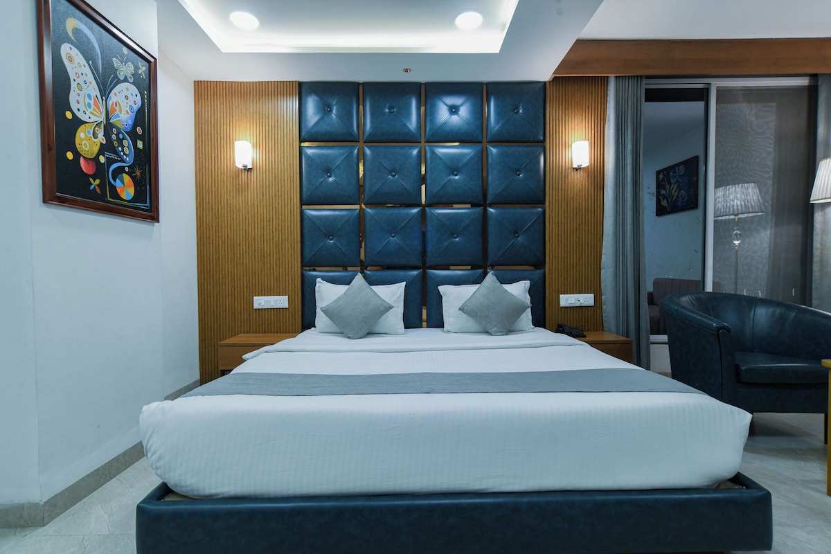 A modern hotel room with a large bed, a headboard with a geometric pattern, a painting on the wall, and a chair.