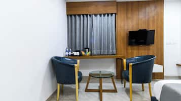 Una habitación de hotel pequeña con cama, dos sillas, una mesita, televisor montado en la pared y ventana con cortinas.