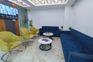 A modern waiting area with yellow chairs, a blue sofa, and a small table with magazines. - Hotel The Grand (Indore)