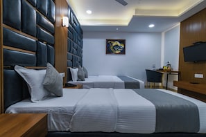 A hotel room with two beds, a desk, a television, and a painting on the wall. - Hotel The Grand (Indore)
