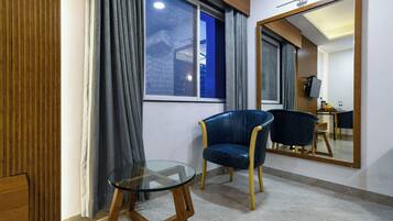 Una habitación con una mesa de vidrio, una silla azul, un espejo grande y un ventanal con cortinas.