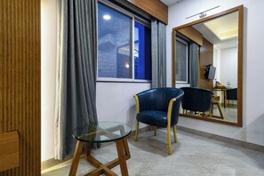 Una habitación con una mesa de vidrio, una silla azul, un espejo grande y un ventanal con cortinas.