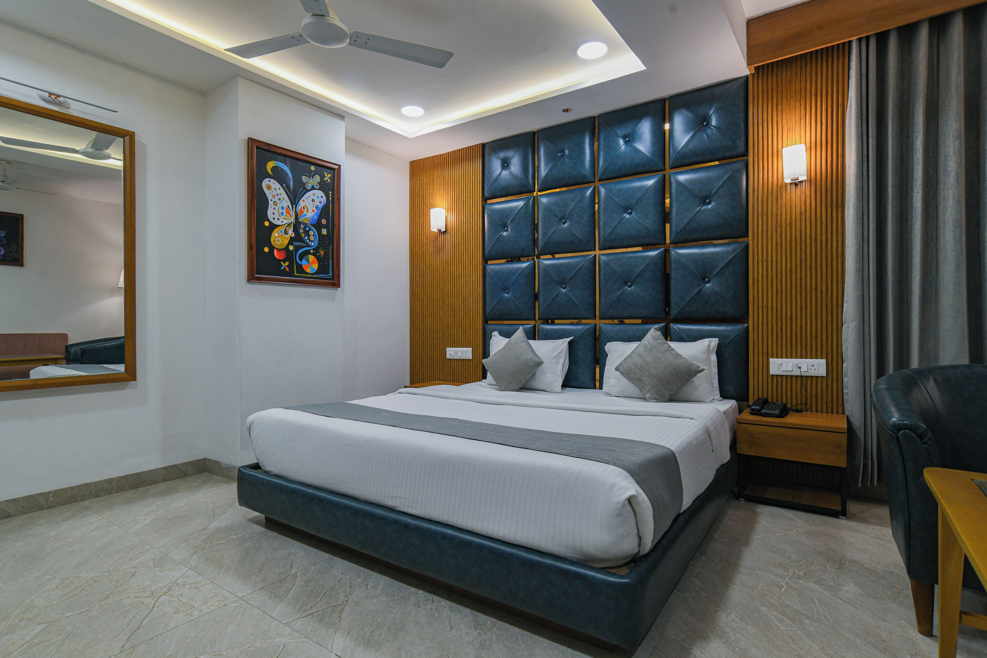 A modern hotel room with a large bed, a ceiling fan, a wall-mounted light, and a bedside table with a phone.
