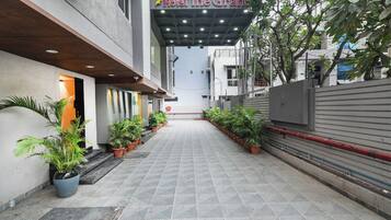 Entrada de hotel con galería techada, plantas en macetas y vista despejada de la fachada del edificio.