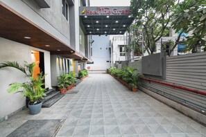 Entrada de hotel con galería techada, plantas en macetas y vista despejada de la fachada del edificio.