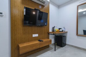 A room with a wooden panel wall, a mounted television, a small wooden bench, a desk with a computer, and a mirror on the wall.