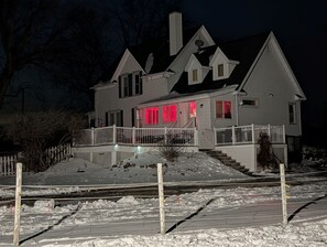 A two-story house with a white exterior, a covered front porch, and a visible staircase leading to the entrance.