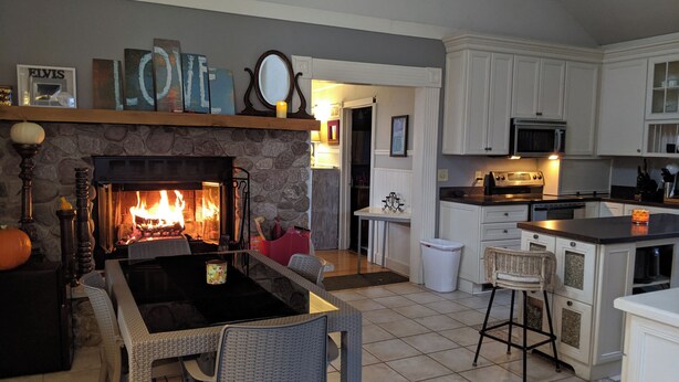 A cozy living room with a fireplace, dining area, kitchen, and a hallway leading to another room. - 4-bedroom updated Farmhouse just 40 minutes north of Milwaukee (Cedar Grove)