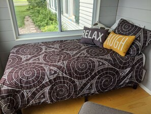 A bedroom with a bed, two pillows, a window, and a view of a garden.