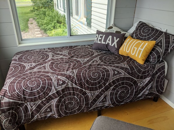 A bedroom with a bed, two pillows, a window, and a view of a garden.