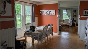 A dining area with a round table, chairs, and a laptop. There is a painting on the wall and a window with a view of greenery. - 4-bedroom updated Farmhouse just 40 minutes north of Milwaukee (Cedar Grove)