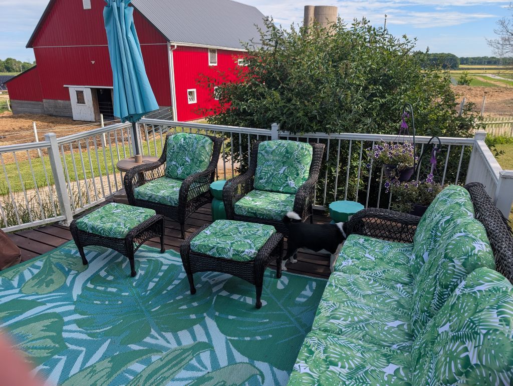 An outdoor deck with wicker furniture, a red barn in the background, and a view of the countryside.