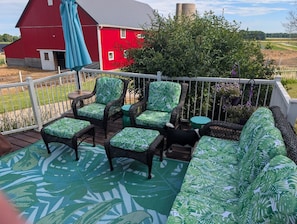 An outdoor deck with wicker furniture, a red barn in the background, and a view of the countryside.