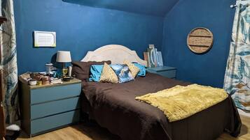 A bedroom with a bed, a nightstand, a lamp, and a wall-mounted round mirror.