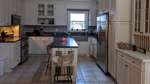 A kitchen with white cabinetry, a central island with seating, a refrigerator, and a window providing natural light. - 4-bedroom updated Farmhouse just 40 minutes north of Milwaukee (Cedar Grove)
