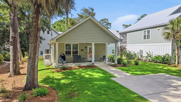 A two-story house with a covered porch, a front yard with a lawn, and a driveway leading to the house. - Our Little Cottage by the Sea - NEW RENTAL (Pawleys Island)