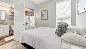 A bedroom with a bed, a bedside table, a lamp, a mirror, and a ceiling fan. - Our Little Cottage by the Sea - NEW RENTAL (Pawleys Island)