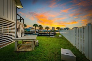 A backyard with a wooden table, a white fence, and a view of a cityscape during sunset. - Boat-Friendly Waterfront Luxury Home in Gulf Shores | Sleeps 19 (Gulf Shores)