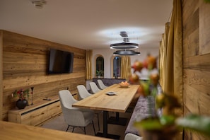 A modern dining area with a wooden table and chairs, a television mounted on the wall, and a unique circular ceiling light fixture. - Modern Suite With Garden or Loggia (Gaschurn)