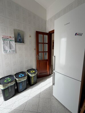 A kitchen with a white refrigerator, a wooden door, and three trash bins labeled for glass, paper, and plastic. - Just a short walk from the Lolli station, a quiet and comfortable apartment (palermo)