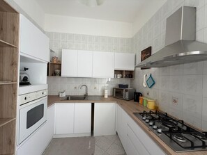 A compact kitchen with white cabinets, a gas stove, a microwave, and a sink. - Just a short walk from the Lolli station, a quiet and comfortable apartment (palermo)