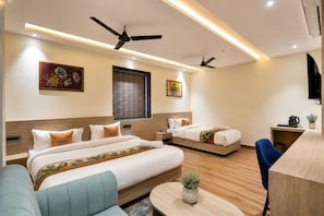 A hotel room with a large bed, a smaller bed, a desk, a chair, a ceiling fan, and artwork on the walls. - Hotel Grand Vista (Gorakhpur)