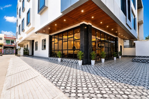 A modern hotel entrance with a tiled walkway, large windows, and potted plants. - Hotel Grand Vista (Gorakhpur)