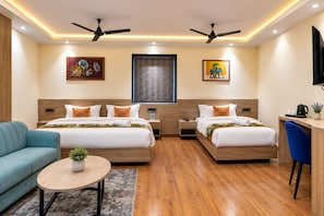 A hotel room with two beds, a desk, a sofa, and ceiling fans. - Hotel Grand Vista (Gorakhpur)