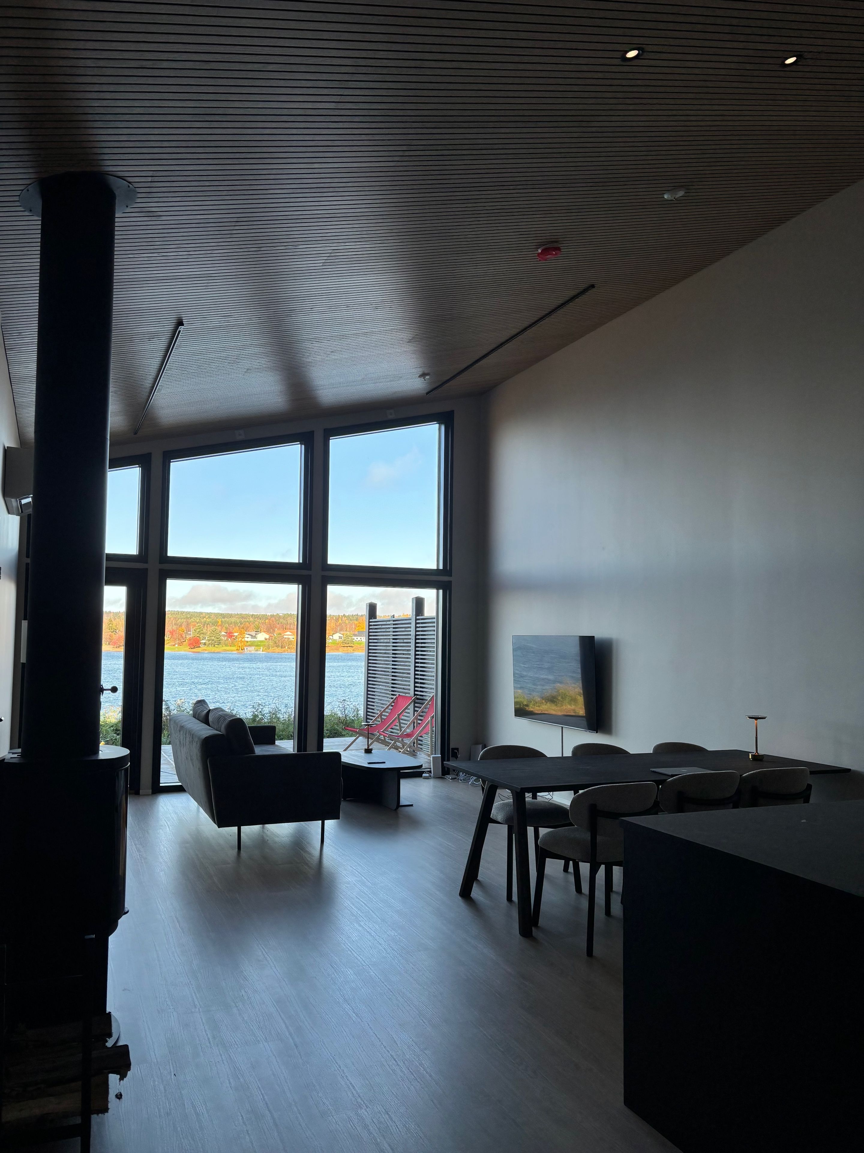 A modern interior with large windows, a fireplace, a dining area, and a view of a lake.