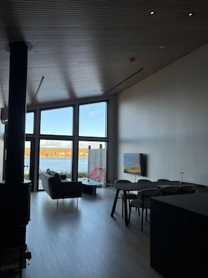 Un interior moderno con grandes ventanales, chimenea, comedor y vistas a un lago.