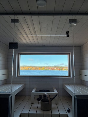 A sauna room with wooden walls, a large window, and a bench.