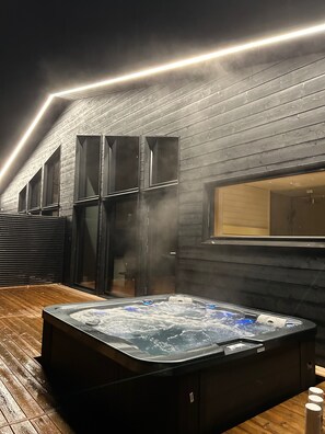 A hot tub with steam rising, surrounded by wooden walls and a sloped ceiling.