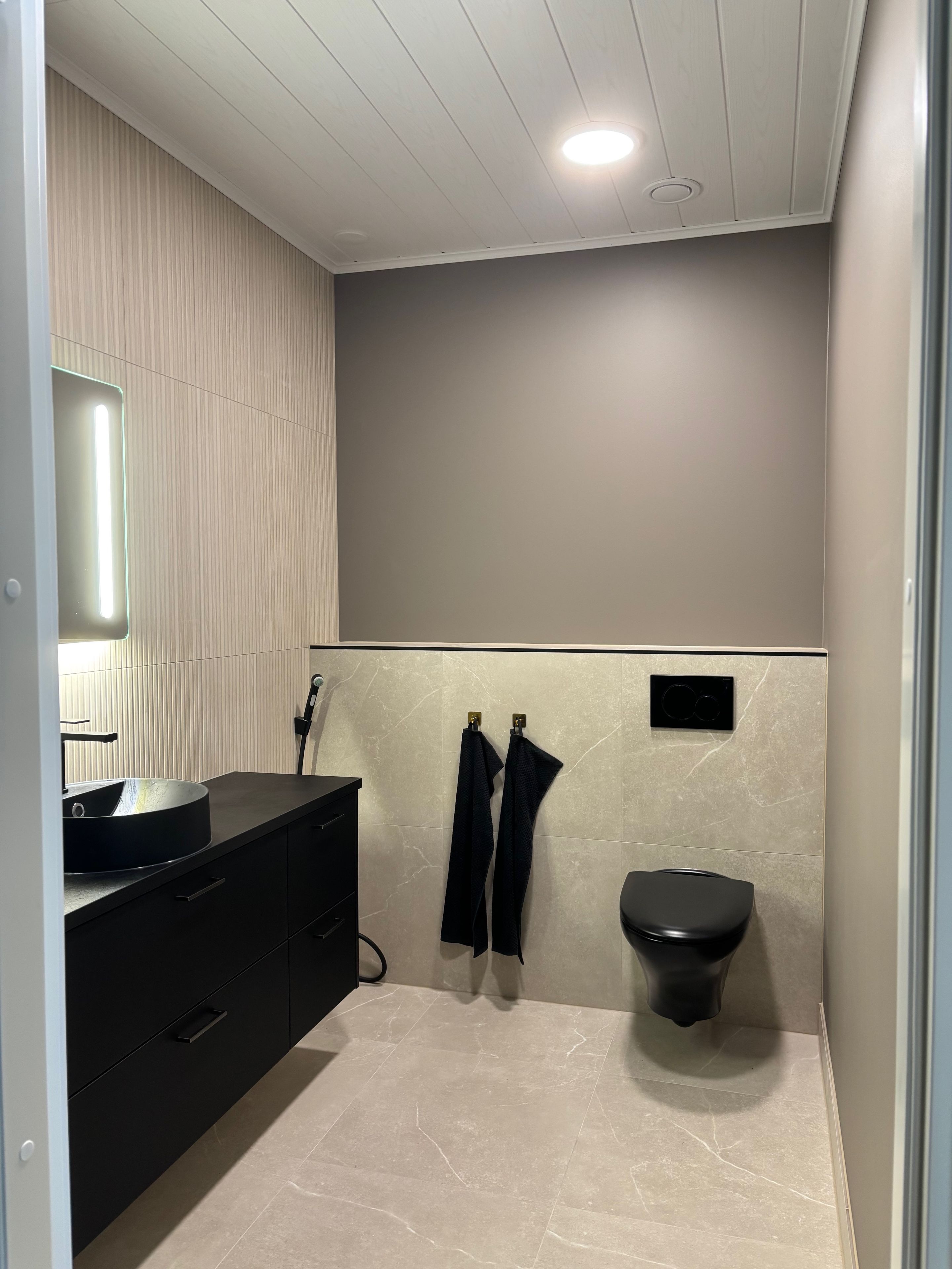 Un baño moderno con un tocador negro, un lavabo redondo, un inodoro y dos toallas colgadas de ganchos.