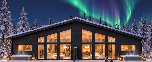 A modern log cabin with large windows, a hot tub, and a view of the northern lights.