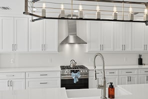 Una cocina moderna con armarios blancos, una campana extractora de acero inoxidable, una estufa a gas y un horno empotrado.