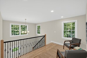 A spacious room with a wooden staircase, a view of greenery through large windows, and a modern light fixture. - Enjoy Quiet Nights With A Fireplace In Bellport 3 Bedroom Home (Bellport)