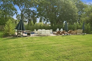 Uma área de estar ao ar livre com piscina, cercada por árvores e equipada com móveis de jardim, incluindo cadeiras e mesas.