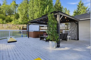 A covered outdoor deck with a hot tub, seating area, and a pergola with string lights. - Pnw Home With Sundance Hot Tub 3 Bedroom Home (Bonney Lake)