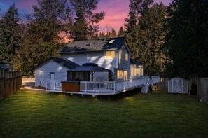 Ein zweistöckiges Haus mit einer Terrasse, einer überdachten Veranda und einem umzäunten Garten.
