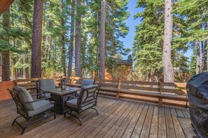 A wooden deck with outdoor furniture, surrounded by tall trees. - Tahoma Family Cabin 3 Bedroom Home (Homewood)